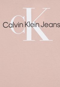Jasnoróżowa bawełniana koszulka z wyraźnym czarnym napisem "Calvin Klein Jeans" oraz dużą białą literą "K". Gładka tekstura i prosty design.