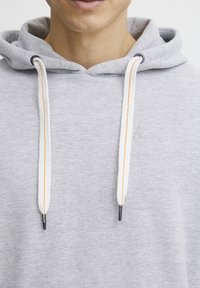 Gray hoodie with a drawstring, featuring white cords with orange accents. Soft texture and a front pocket. Subtle logo embroidered on chest.
