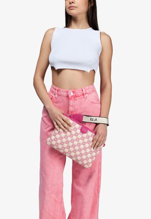 Borsa a tracolla rosa con sfondo cream a motivo, chiusura con zip e una tracolla rosa con logo. Il modello indossa un top corto a coste bianco e jeans rosa.