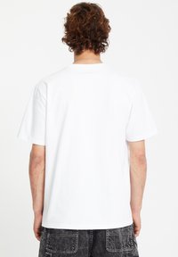 White cotton t-shirt with a relaxed fit, short sleeves, and a round neckline. Back view shows smooth texture and simple design.