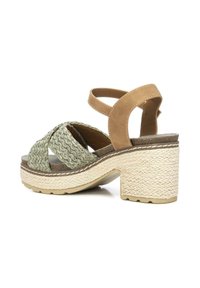 Sandalias con tiras verdes trenzadas y una correa de tobillo color marrón, con un tacón grueso beige y una plataforma texturizada, diseñadas para ofrecer comodidad y estabilidad.