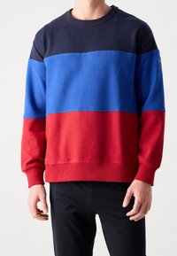 Sudadera bicolor con paneles en azul marino, azul y rojo. Fabricada con material suave, con puños y dobladillo acanalados. Corte casual y ligera.