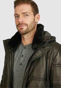 Braune Lederjacke mit einer gefütterten Kapuze aus schwarzem Fell, ausgestattet mit einem Reißverschluss und Druckknopfverschluss, sowie einem grauen Henley-Shirt darunter.