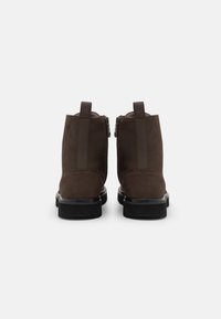 Botines de ante marrón con un acabado suave, cremalleras traseras y lengüetas; cuentan con una suela negra gruesa para mayor altura.