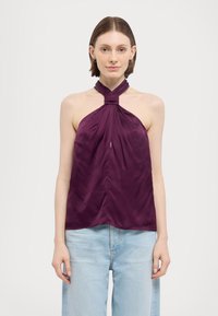 Top halter in satin Puris di colore viola profondo, con design del collo annodato e silhouette fluida, indossato con jeans a gamba larga di colore blu chiaro.