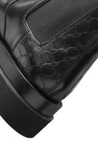 Botte en cuir noir avec un motif texturé, un panneau latéral élastique et une semelle épaisse noire pour la stabilité et la continuité du design.