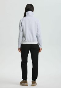 Light gray fleece jacket with high collar, ribbed hem, and long sleeves, paired with black pants and brown hiking shoes.
