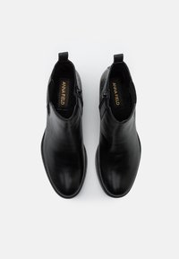 Botines negros de cuero con acabado liso, cremalleras laterales y detalles texturizados. Punta redondeada y tacón bajo apilado.