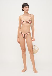 Svītrots bikinis sarkans un krēmkrāsā, ar regulējamiem siksniņām, bandeau tipa augšdaļu un augsto vidukļa apakšdaļu. Komplektā ietilpst austs rokassomu.