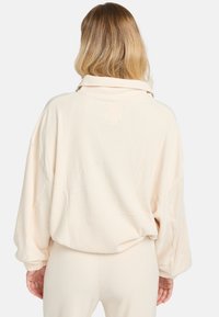 Cremfarbener, gerippter Oversized-Pullover mit umgeschlagenem Kragen und langen Ärmeln, der einen lockeren Schnitt und subtile Nähdetails aufweist.