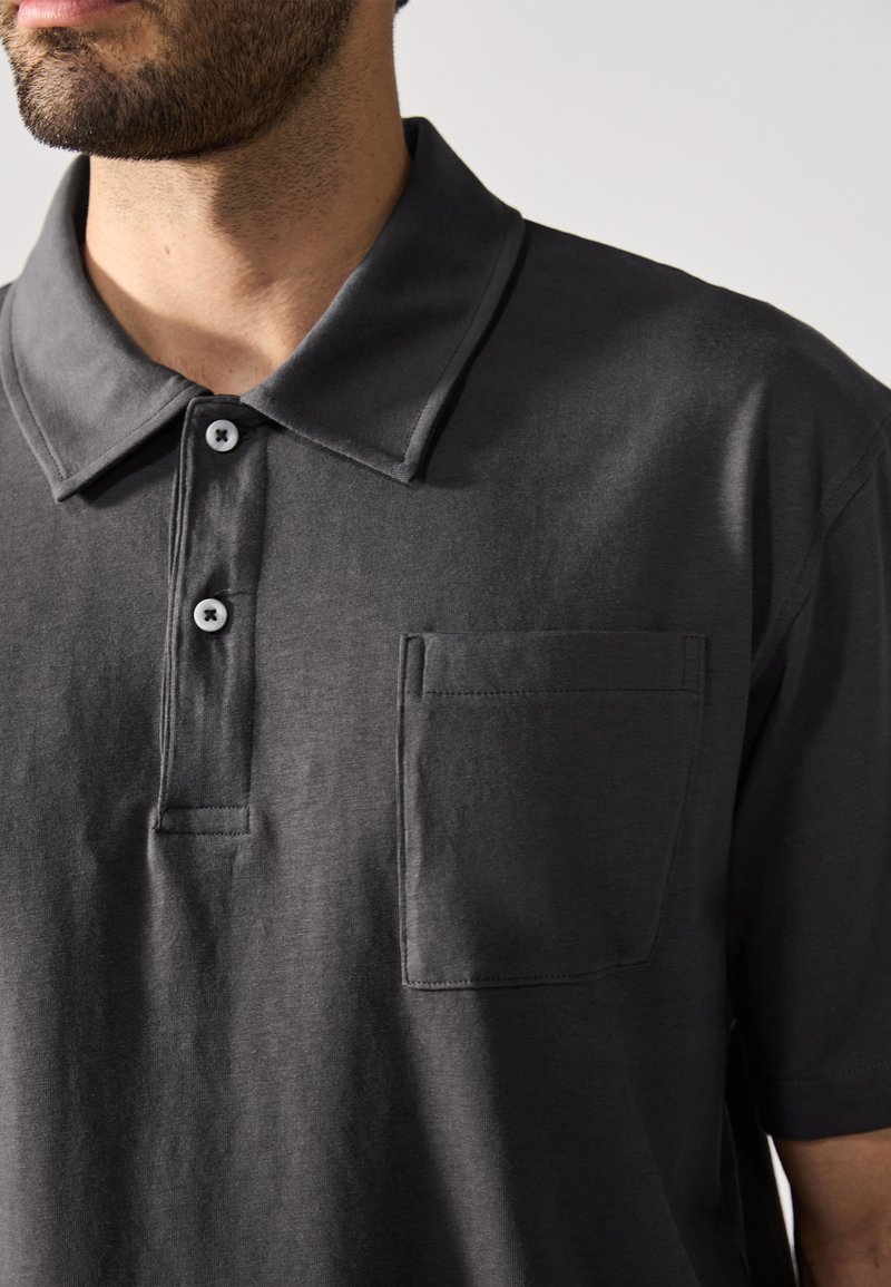Polo shirt grigio scuro realizzato in tessuto morbido, con colletto classico, tre bottoni e taschino sul lato sinistro.