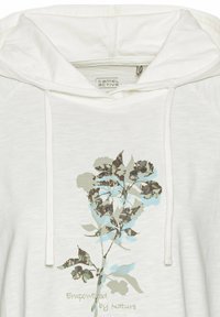 Hvid hættetrøje med snore og et blomsterprint i nuancer af grøn og blå. Teksten lyder "Støttet af Naturen." Blødt stof.