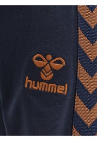 Marineblaues Gewebe mit orangefarbenem gesticktem Logo und einer Zickzackmusterstruktur an der Seite. Glatte Oberfläche, Details betonen die Markenidentität.