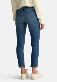 Blå denim skinny jeans med hög midja, med två bakfickor och rå fåll. Matchas med krämfärgade snörskor.