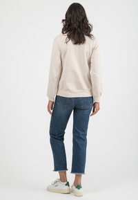 Felpa beige con maniche lunghe, scollo rotondo e polsini a coste, abbinata a jeans blu con orlo tagliato e sfilacciato e sneakers bianche.