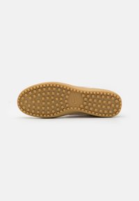 Semelle de chaussure avec des clous carrés en caoutchouc et logo Nike embossé au centre sur une semelle extérieure marron clair sur fond uni.