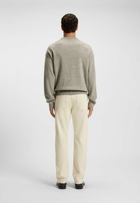Maglione grigio a maglia con scollo rotondo, maniche lunghe e polsini a costine, abbinato a pantaloni a gamba dritta color crema e scarpe scure.