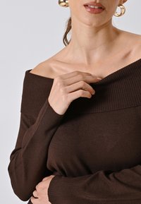 Brauner, schulterfreier Pullover aus geripptem Strickmaterial mit langen Ärmeln und weitem Ausschnitt. Glatte Textur mit figurschmeichelndem Design.