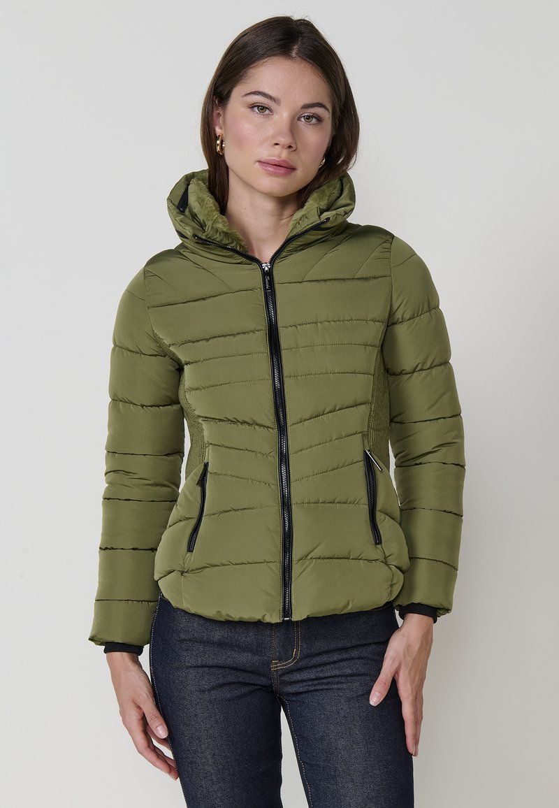 Chaqueta acolchada verde oliva con cierre delantero, diseño ajustado, capucha y detalles en cremallera negra. Presenta costuras diagonales y bolsillos laterales.