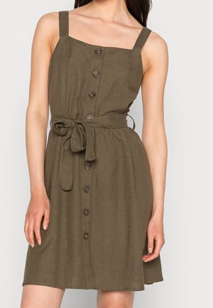 Robe sans manches vert olive avec boutons sur le devant et ceinture nouée à la taille, portée par une femme des épaules jusqu'à mi-cuisse.