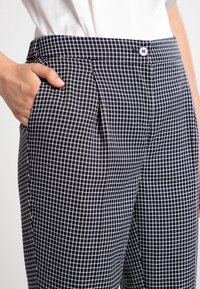 Black and white checkered trousers with a flat front, side pockets, and a button closure at the waist, featuring a smooth, structured fabric.