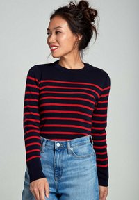 Maglione a righe blu navy e rosso con scollatura a girocollo e dettagli di bottoni sulle spalle, abbinato a jeans di denim blu a vita alta.