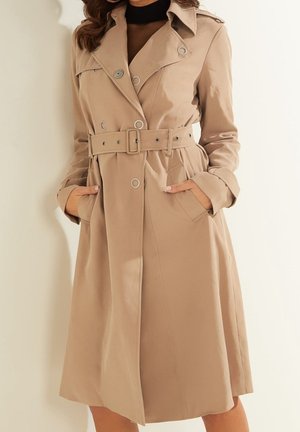 Manteau beige en tissu lisse, à double boutonnage, avec une taille ceinturée et de grandes poches avant.