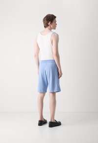 Lyseblå shorts med elastisk linning, glatt stoff og rullet kant; sammen med en hvit topp og svarte sko.