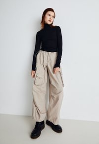 Svart genser med høy hals, beige cargo-bukser med sidelommer og svarte snørebåndsstøvler. Outfiten har en avslappet silhuett og uformelle materialer.