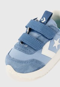 Baskets bleues avec un mélange de tissus lisses et de textures en daim. Bandes Velcro et un logo d'étoile blanche bien en vue sur le côté. Semelle blanche.