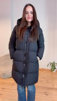 Sort pufferjakke med lynlås foran, hætte og sidelommer. Har et quiltet design og glat overflade. Bæres over blå jeans.