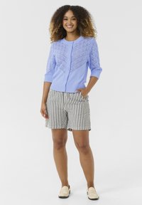 Svetlo modra pletena jopica z čipkastim vzorcem, v kombinaciji s kratkimi hlačami v črno-belih črtah. Model nosi kremne loaferje, roke v žepih.