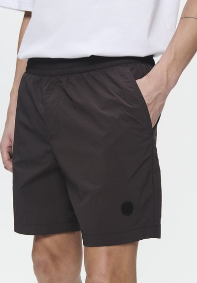 Shorts marron foncé en tissu léger, dotés d'une taille élastique, de poches latérales et d'un patch logo au bas.