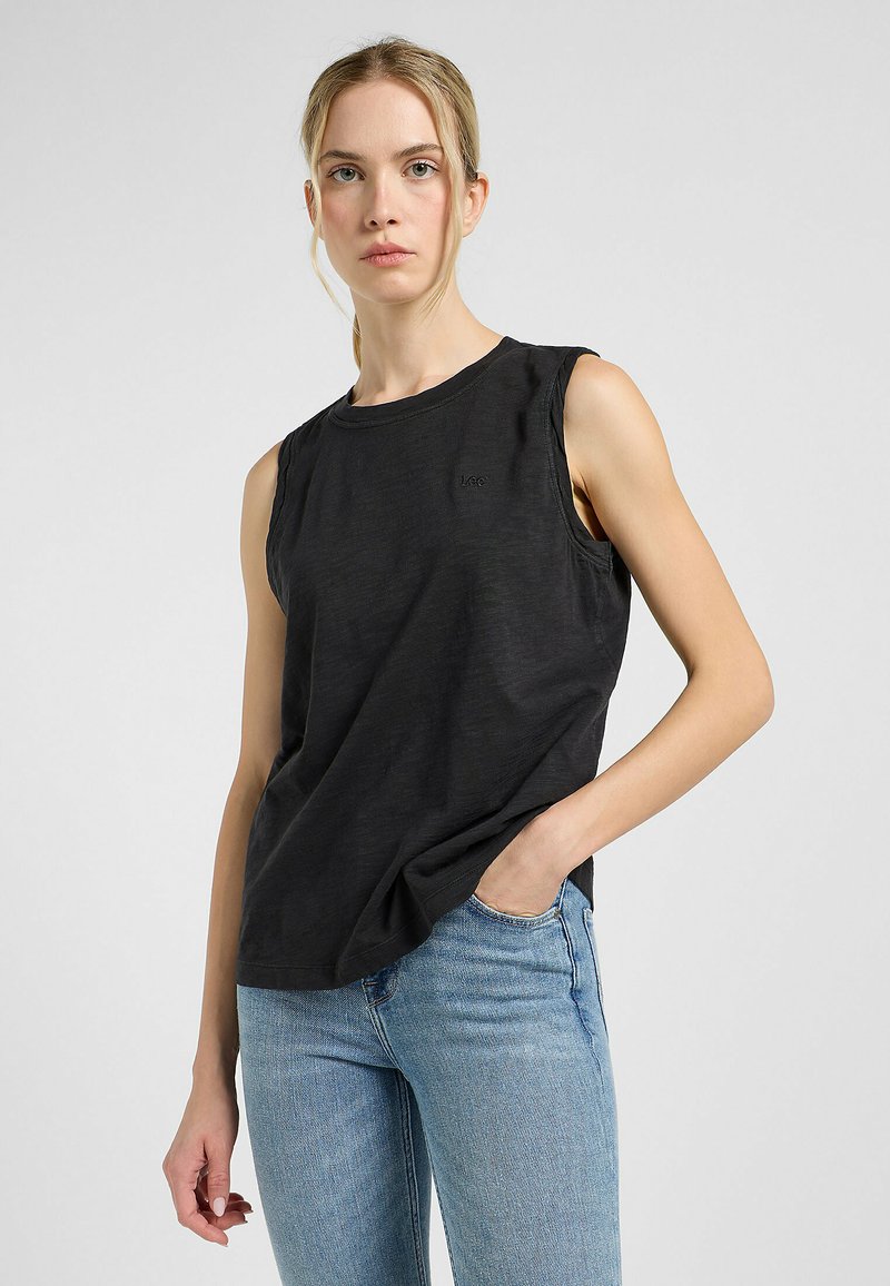 Sort ærmeløs top med en rund halsudskæring, lavet af blødt stof; har diskret branding på brystet og en afslappet pasform, parret med blå jeans.