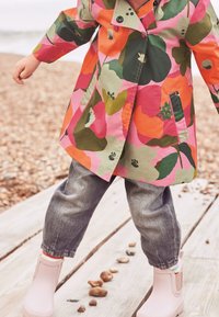 Imperméable floral coloré avec des motifs roses, verts et oranges. Associé à un pantalon en denim gris et des bottes imperméables rose pâle.