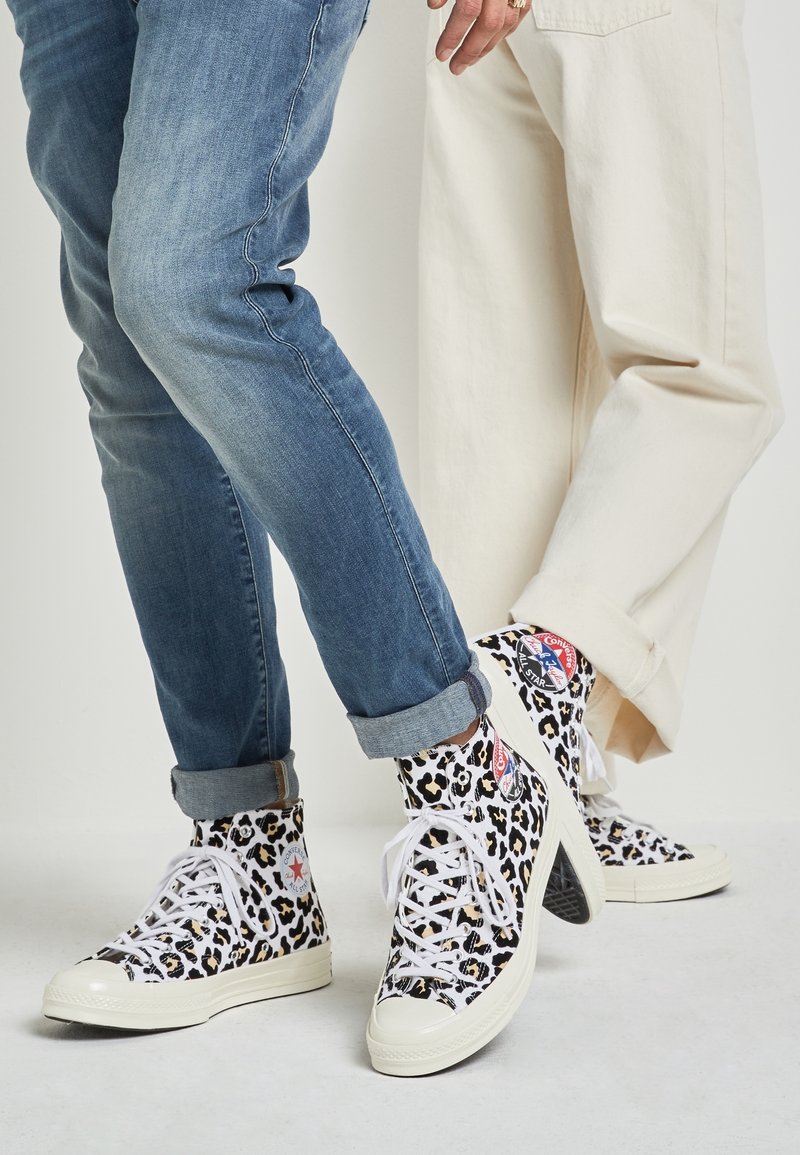 Zapatillas altas con un estampado de leopardo en blanco y negro, cordones blancos, suelas de goma y logotipos de contraste. Jeans de corte recto con dobladillo visible.