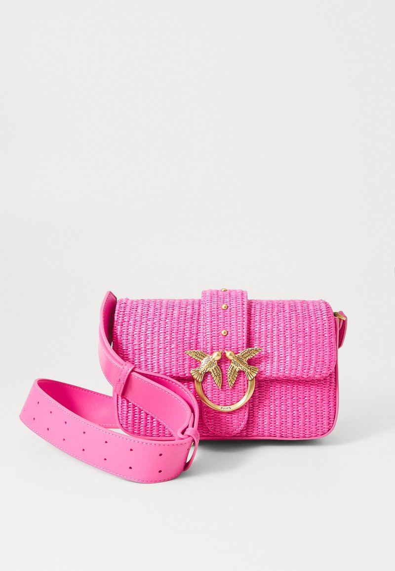 Saco trançado rosa com superfície texturizada, acessórios em forma de folha de palmeira dourada, alça de couro ajustável e fecho de pressão. Apresenta tachas decorativas.