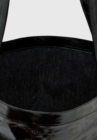 Sac à main noir brillant avec deux anses et intérieur en tissu lisse, vu de dessus en se concentrant sur le haut ouvert et la doublure intérieure.