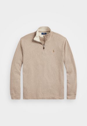 Pull beige à manches longues avec fermeture éclair quart de zip, col montant, petit logo brodé sur la poitrine gauche, posé à plat sur fond blanc.