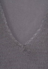 Gros plan sur un tissu gris texturé avec un décolleté en V et de fines coutures.