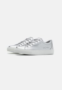 Une paire de baskets basses en argent avec des semelles en caoutchouc blanches et des lacets gris, présentant un texte logo discret sur le côté.