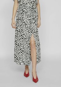 Gonna leopard print a lunghezza intera in bianco e nero con uno spacco laterale, realizzata in tessuto leggero. Indossata con tacchi a punta rossi.