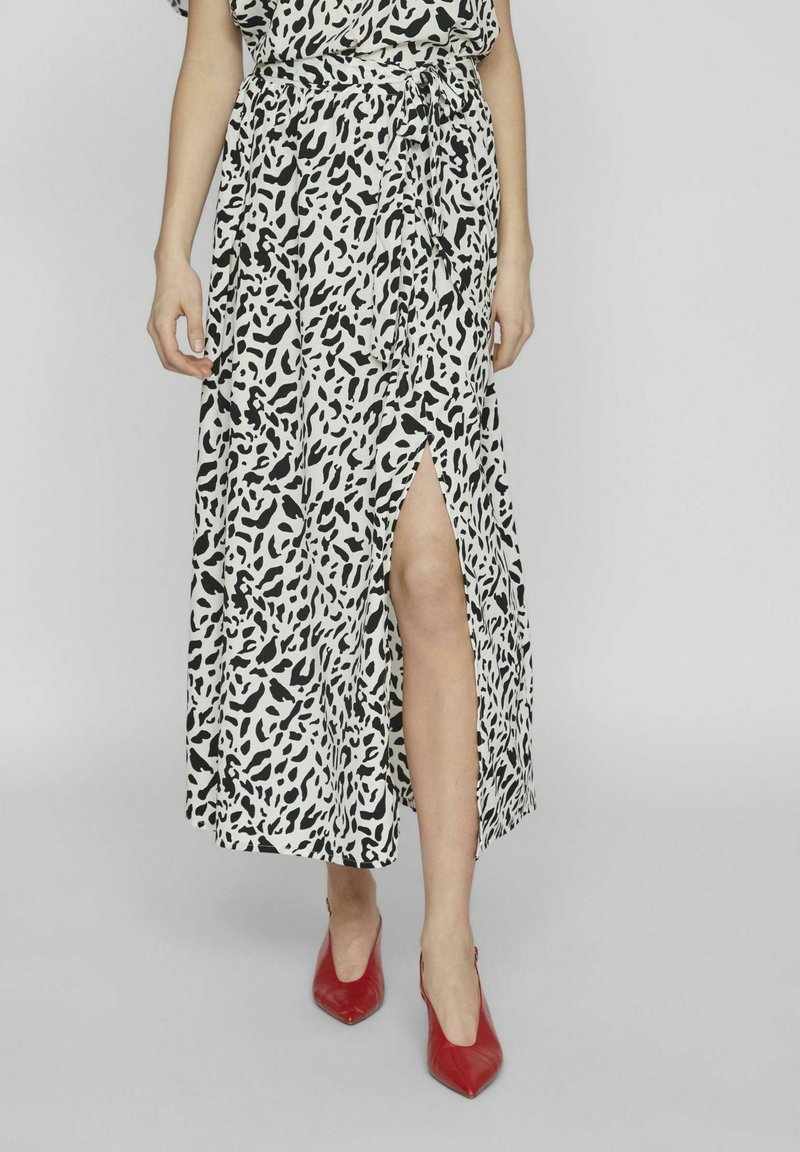 Gonna leopard print a lunghezza intera in bianco e nero con uno spacco laterale, realizzata in tessuto leggero. Indossata con tacchi a punta rossi.