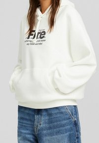 Sudadera blanca con capucha fabricada en una mezcla de algodón, que presenta un bolsillo frontal y texto impreso en negro. Corte holgado con puños y dobladillo acanalados.