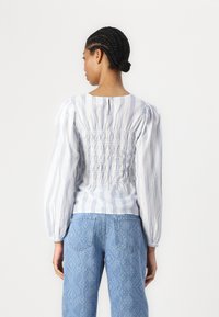 Lyseblå og hvit stripete topp med smocket bak og puffermer, kombinert med lyseblå mønstrede jeans. Tettsittende i midjen.