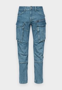 Pantalones cargo de mezclilla azul claro con múltiples bolsillos, detalle con cremallera y un ajuste ajustado. Tejido texturizado con costuras visibles.
