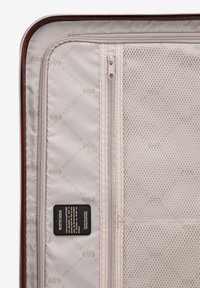 Large suitcase interior with beige fabric lining, zippered compartments, mesh pocket, and brand label detailing.