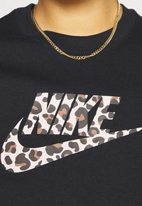 Svart sweatshirt med en stor Nike-logotyp i ett leopardmönster med bruna och grå accenter. Guldhalsband synligt.
