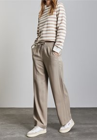 Sweatshirt beige à rayures avec un col rond, associé à un pantalon beige ample avec une taille élastique et des poches latérales. Baskets blanches.