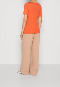 T-shirt arancione a maniche corte in tessuto texturizzato abbinato a pantaloni beige chiaro a gamba larga, caratterizzati da una vestibilità morbida e dettagli minimi.